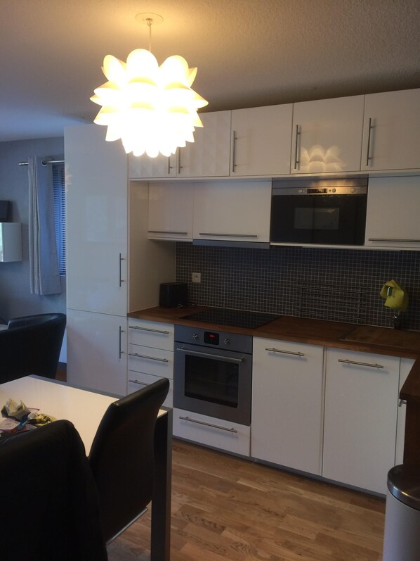 A modern kitchen with white cabinets, a wooden countertop, and a black tiled backsplash.