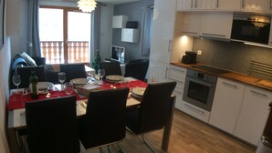 En matplats med ett bord för fyra personer, stolar, ett kök med moderna vitvaror och en balkong med ett räcke.