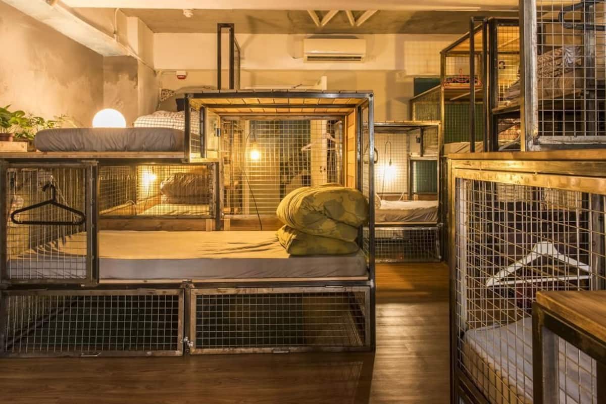 A room with multiple bunk beds, each enclosed in metal cages, and a small bed with a pillow.