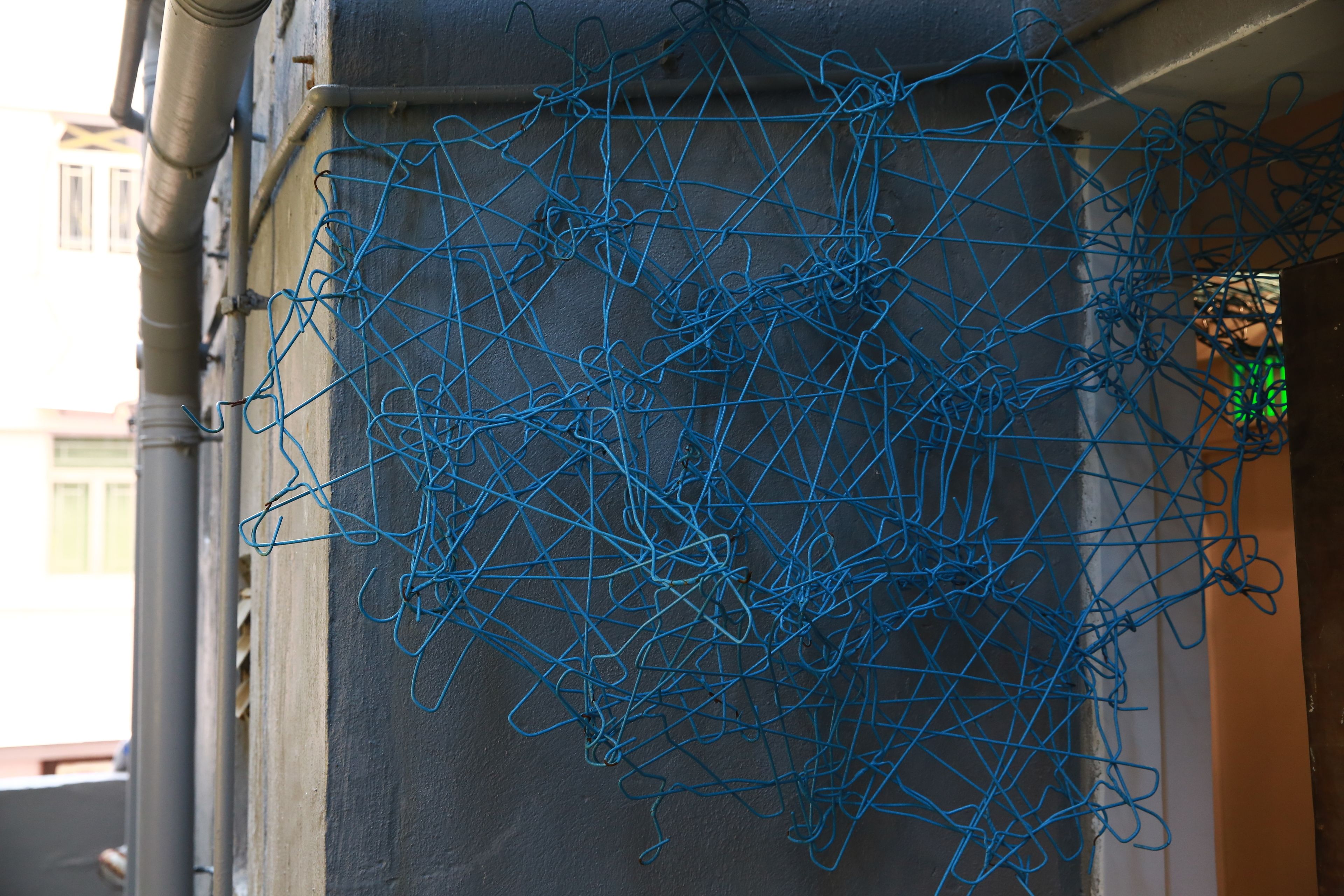 A tangled blue wire against a building wall.