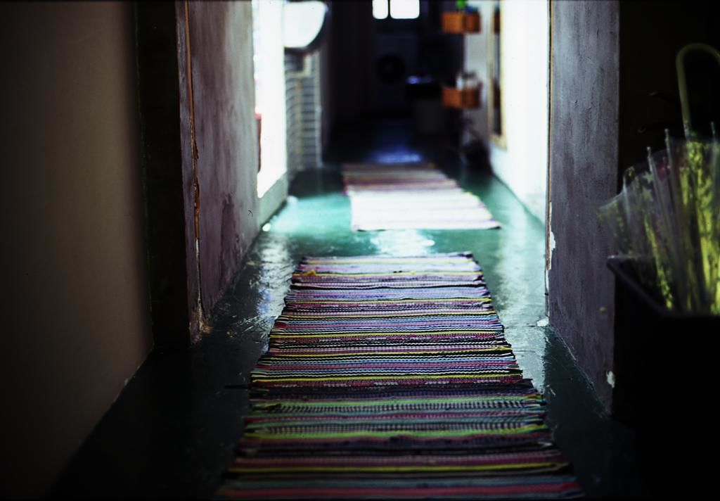Un couloir étroit, orné d’un tapis rayé aux couleurs vives, mène à une pièce sombre.
