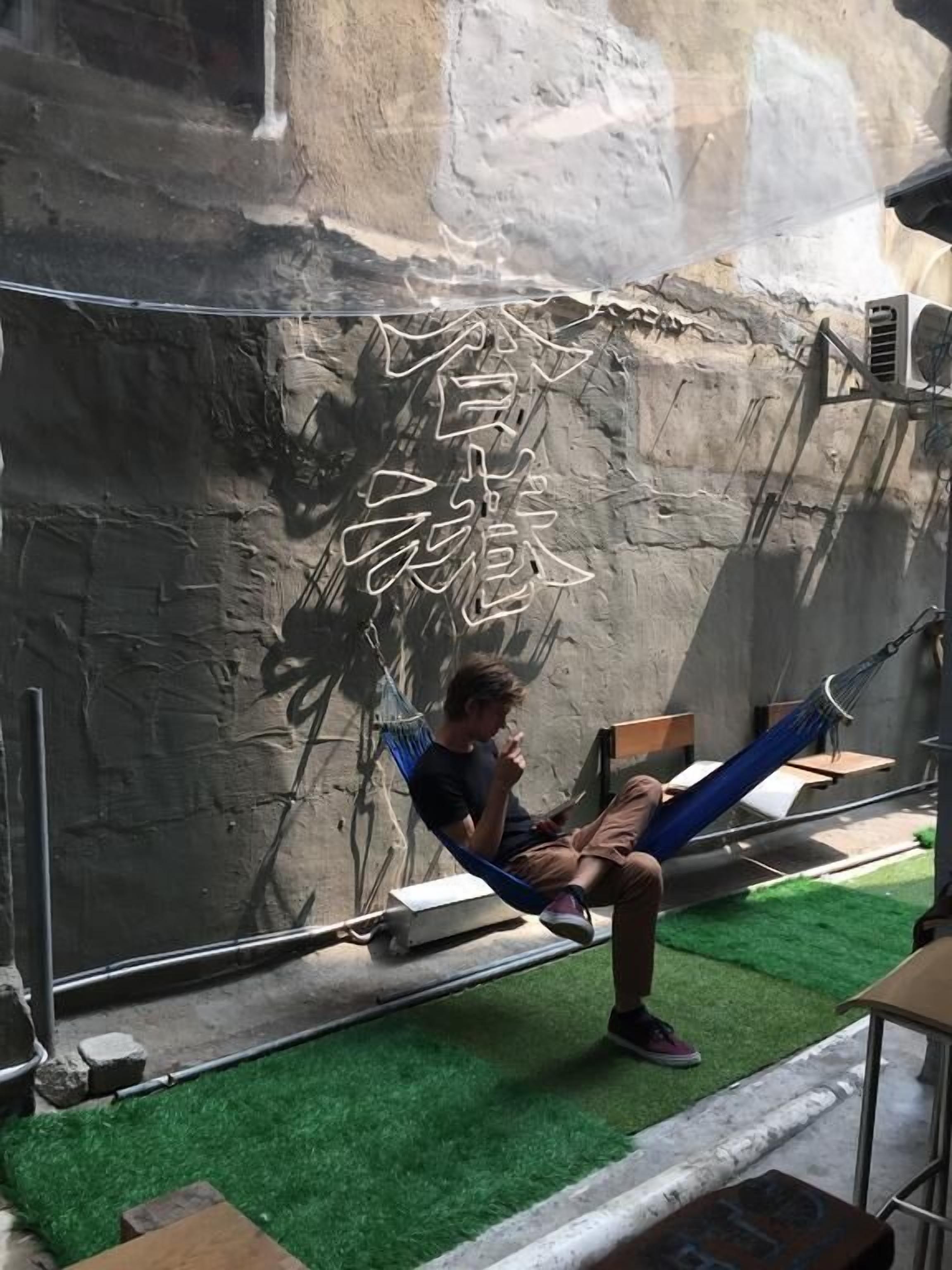 A person sitting on a hammock in a room with a stone wall and artificial grass.