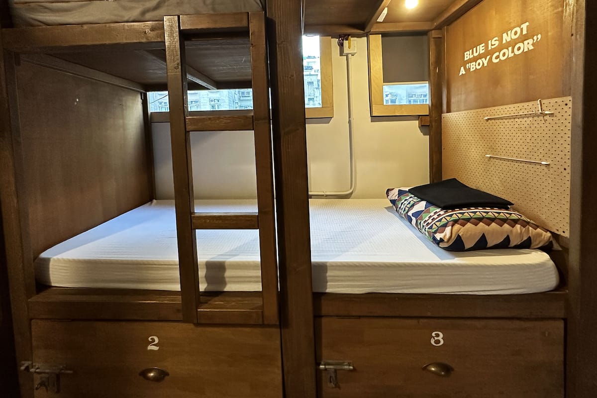 A bunk bed with a ladder, two drawers, a pegboard, and a wall sign stating "BLUE IS NOT A 'BOY COLOR'".