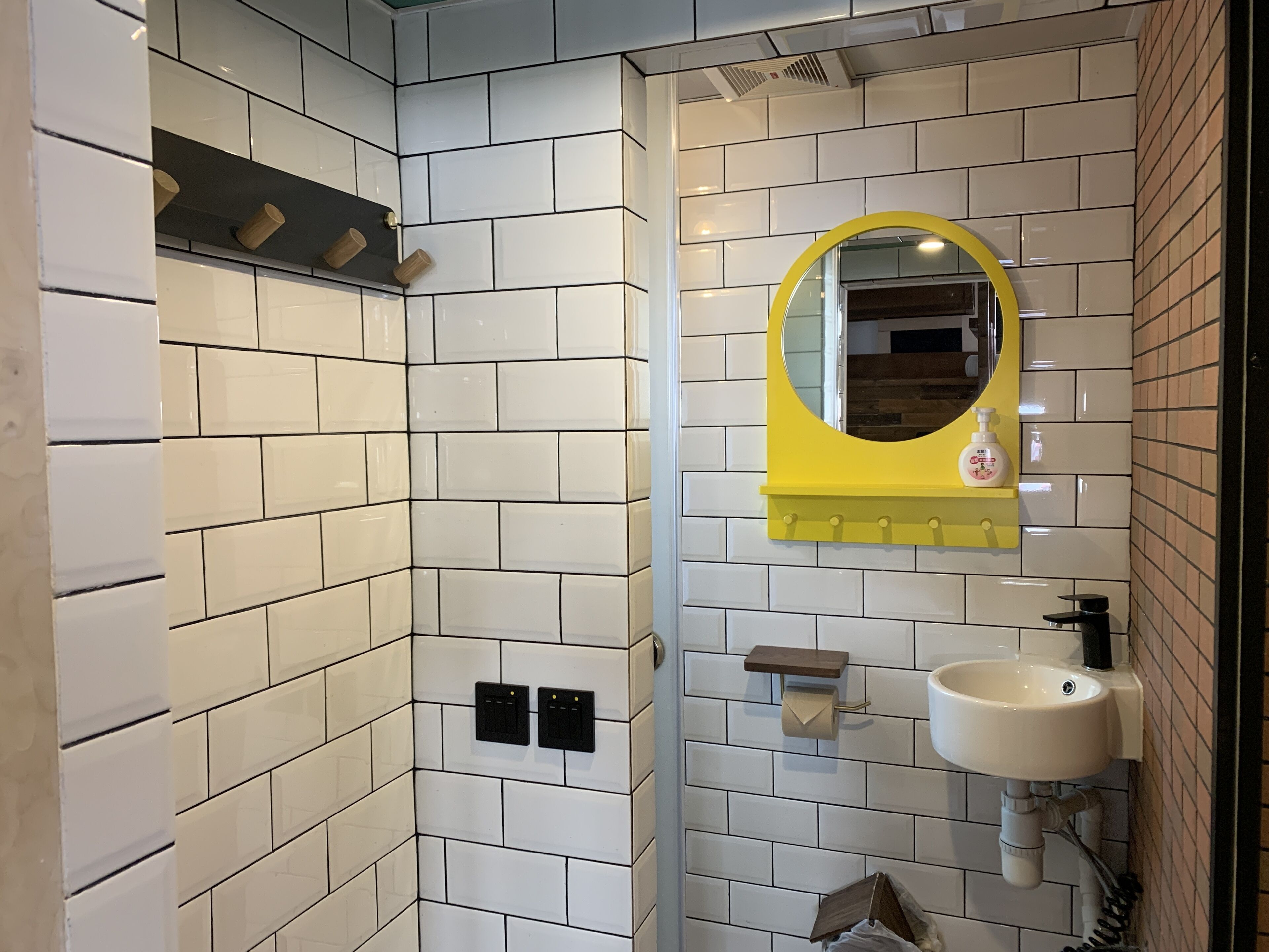 A bathroom with white tiled walls, a yellow-framed mirror, a sink, and a shower area.