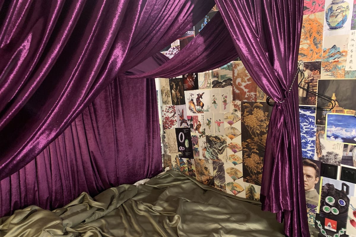 A room with a bed, purple curtains, and a wall decorated with various artworks.