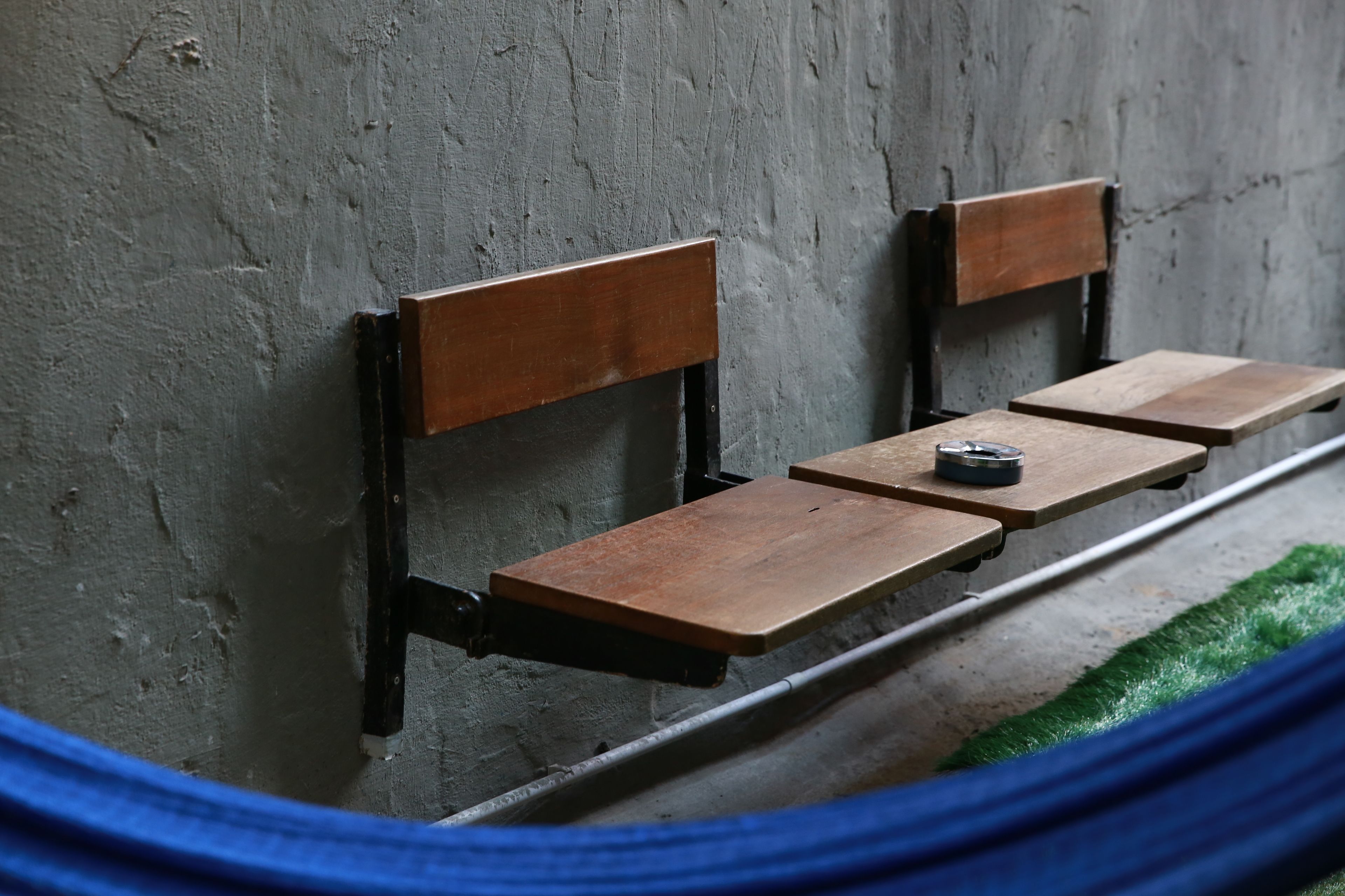 A bench with a metal frame and wooden seat against a textured wall.