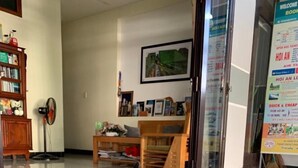 A black dog on a leash in a room with a tiled floor, a wooden cabinet, a fan, and a framed picture on the wall. - Fireworks Homestay (Da Nang)