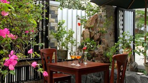 A wooden table with chairs, surrounded by potted plants and a stone wall. - Fireworks Homestay (Da Nang)