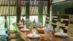 A long wooden dining table set for a meal with plates, glasses, and a basket of bread. - The Manipura Luxury Estate & SPA 730sqm Living Area, 20m Iinfinity Pool (Ubud)