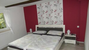 Ein Schlafzimmer mit einem Bett, zwei Nachttischen, einem Fenster und floralem Tapetenmuster.
