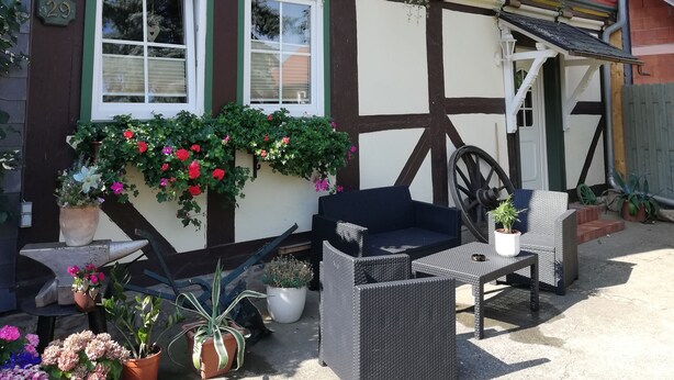 Ein Fachwerkhäuschen mit Blumenkästen an den Fenstern und einer Terrasse mit Gartenmöbeln.