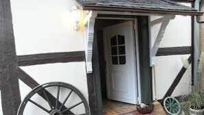 Ein traditionelles Fachwerkhäuschen mit weißer Tür, einem großen Holzrad und einer kleinen Stufe zum Eingang.