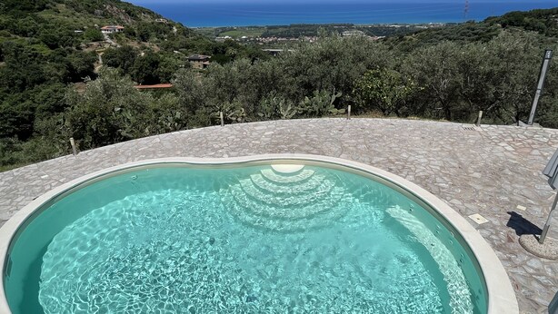 Une piscine dotée d’une plage en pierre, entourée d’une végétation luxuriante et offrant une vue sur un paysage côtier.
