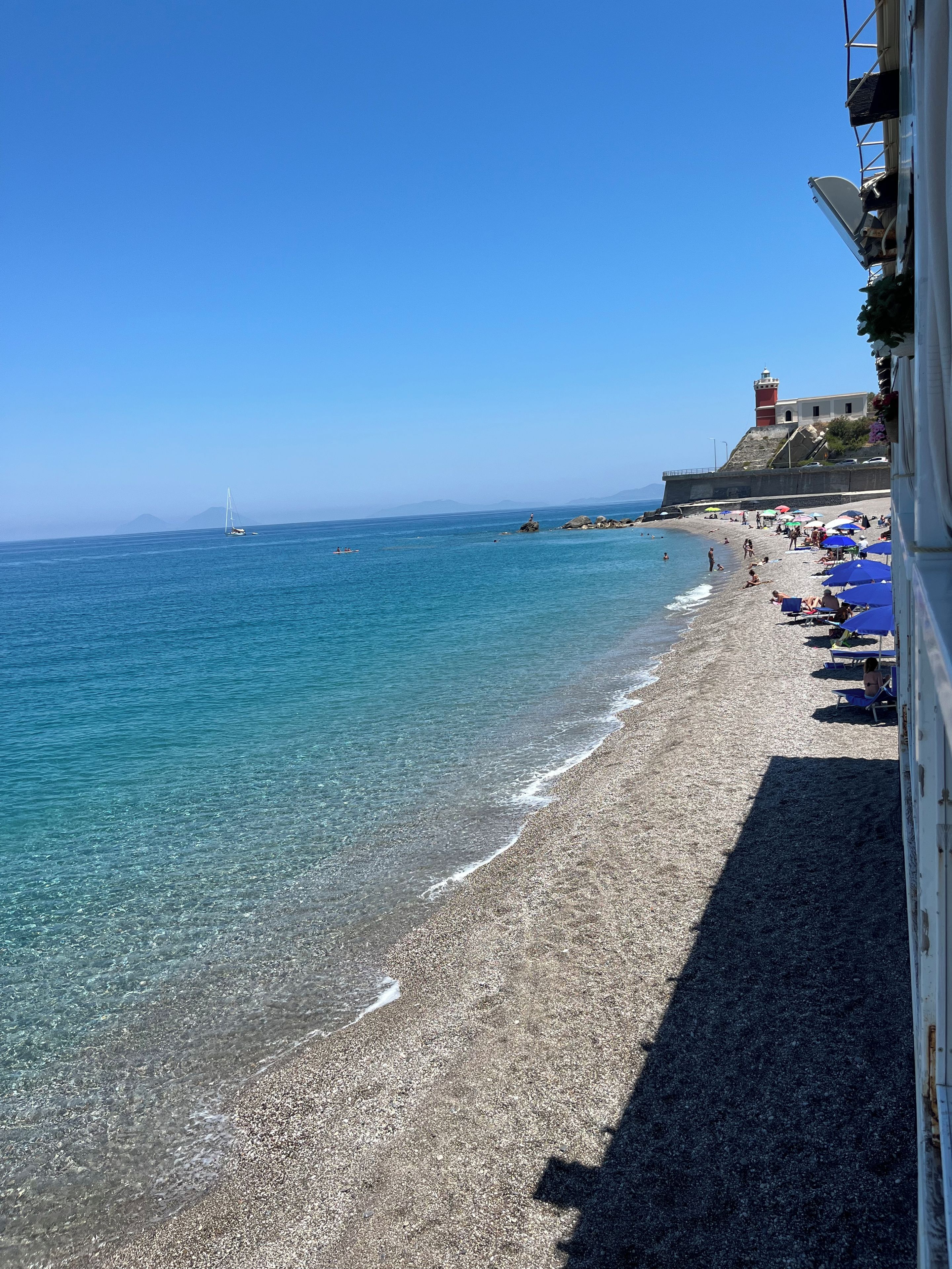 Une plage à l’eau claire, un phare et un bâtiment doté d’un balcon.
