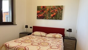 A bedroom with a bed, two bedside tables, a window, and a wall-mounted picture.