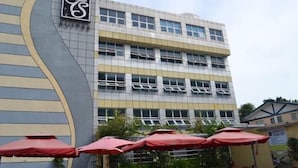 A multi-story hotel with a modern design, featuring a prominent logo on the facade. - Trace Suites by SMS Hospitality (Los Banos)