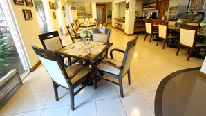 A dining area with a large table, chairs, and a view of the outdoors. - Trace Suites by SMS Hospitality (Los Banos)