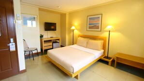 A hotel room with a bed, bedside lamps, a desk, a chair, a TV, and a bench. - Trace Suites by SMS Hospitality (Los Banos)