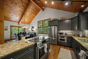 Une cuisine dotée de plans de travail en granit, d’appareils électroménagers en acier inoxydable et de poutres en bois au plafond.