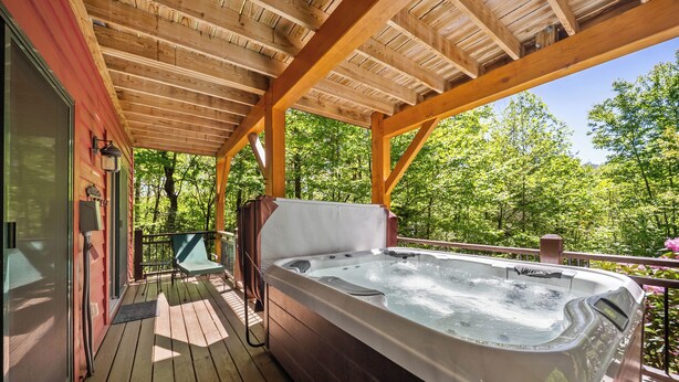 A wooden deck with a hot tub, a chair, and a view of a forest.