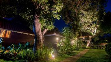 A well-lit garden with a wooden house, a pathway, and various plants.