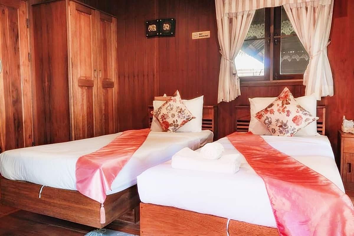 Ein Zimmer mit zwei Holzbetten, jeweils mit weißer Bettdecke und rosafarbenem Laufen. Es gibt einen Holzschrank und ein Fenster mit Vorhängen.
