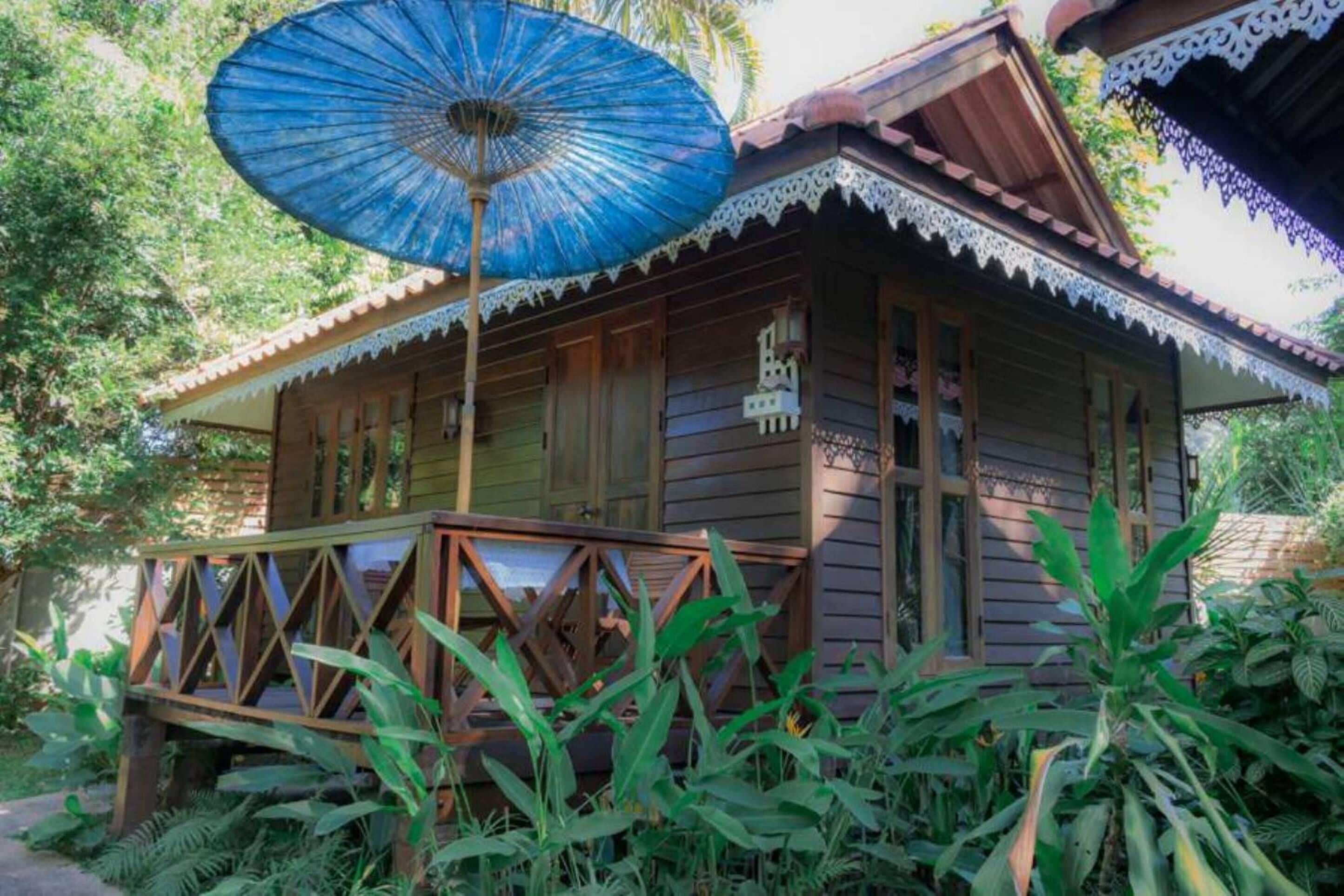 A wooden house with a porch, surrounded by lush greenery.