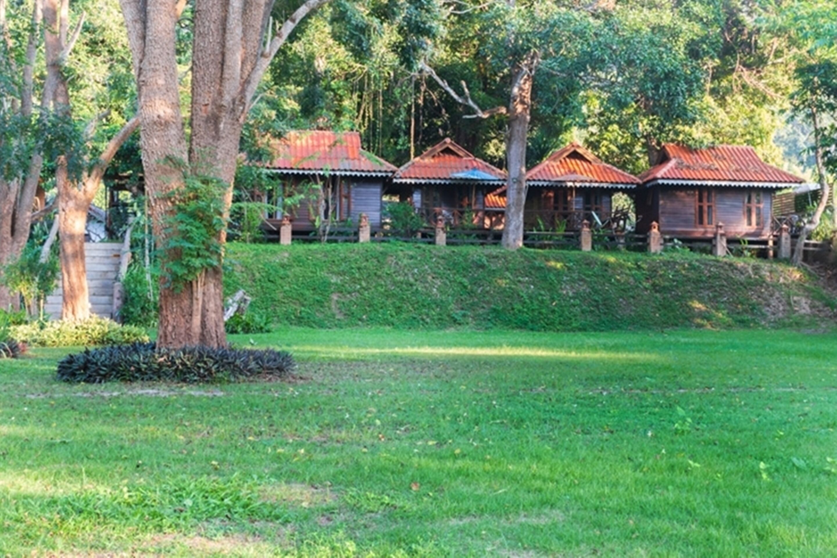 A row of wooden cabins with red roofs, surrounded by lush greenery and trees.