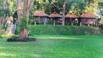 A row of wooden cabins with red roofs, surrounded by lush greenery and trees.