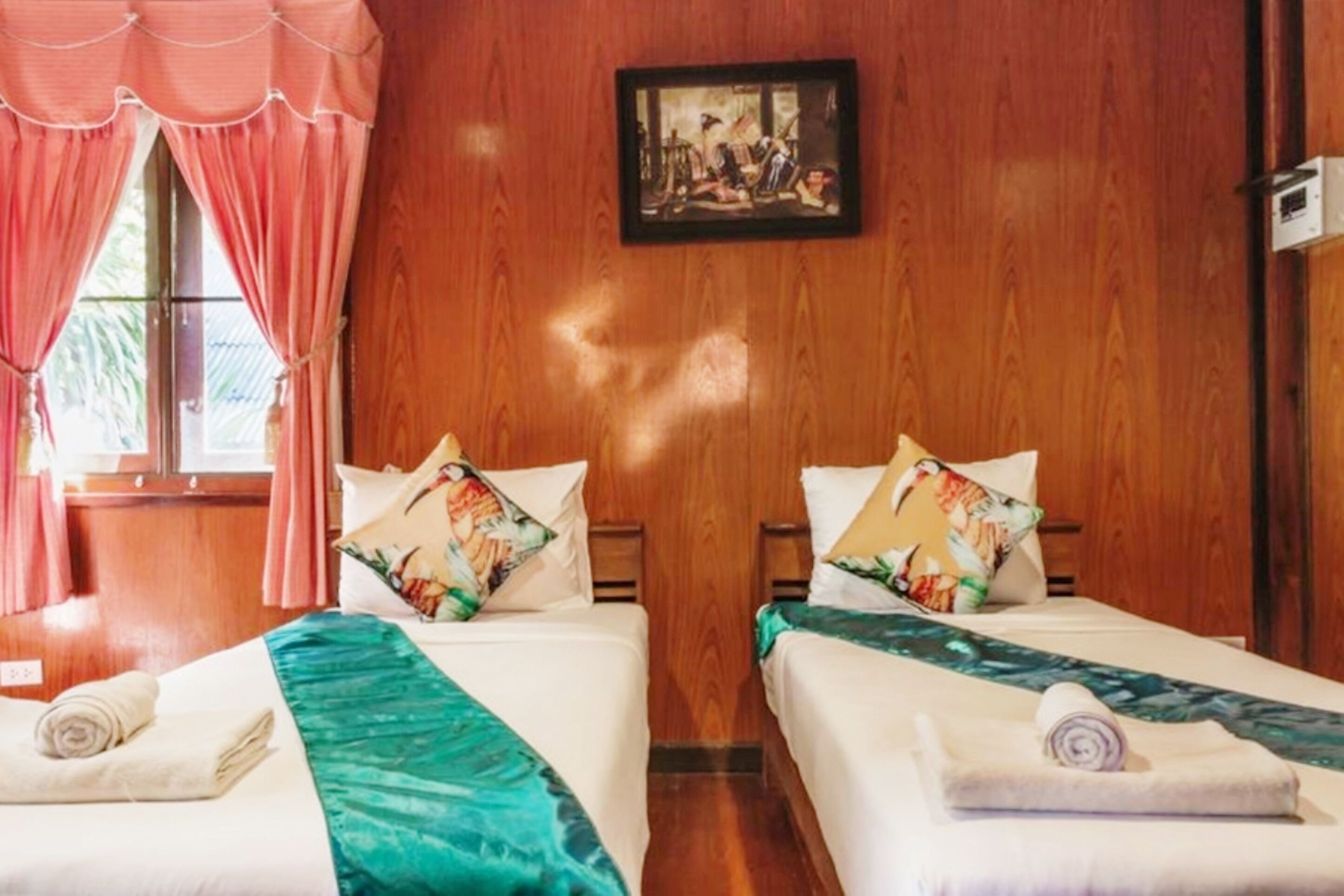 Habitación de hotel con dos camas, paredes de madera, un cuadro y una ventana con cortinas.