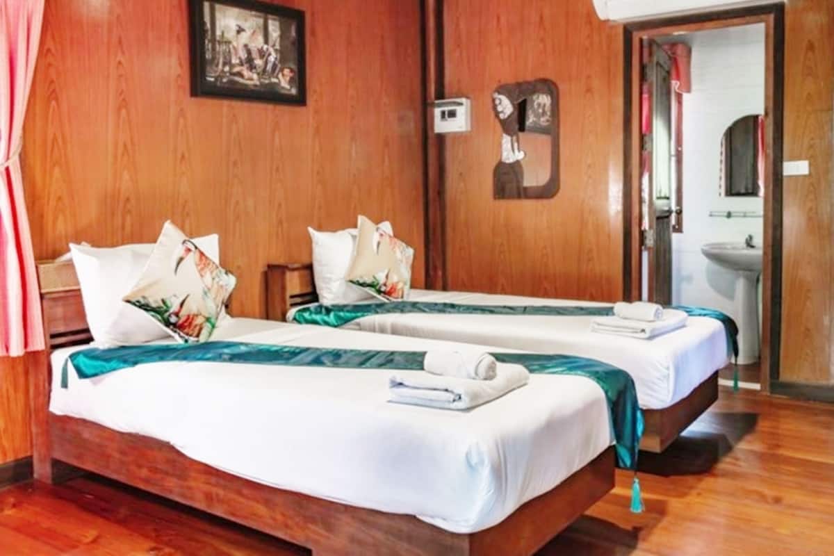 Ein Hotelzimmer mit zwei Betten, Holzwänden, einem Gemälde, einem Spiegel und einem durch eine offene Tür einsehbaren Badezimmer.