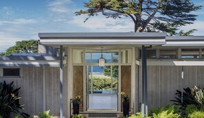 A modern house with a large glass door leading to a balcony, surrounded by greenery. - Cypress Point - Pebble Beach House - Oceanview Luxury at Cypress Point (Pebble Beach)