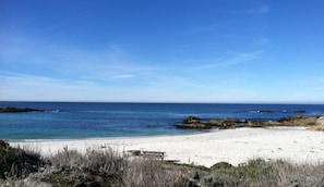 Een strand met helderblauw water, wit zand en rotsachtige uitstulpingen.