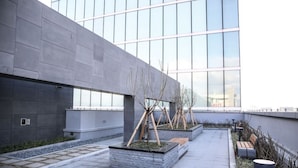 Un espace extérieur moderne agrémenté de jardinières, de bancs et d’un chemin menant à un bâtiment doté de grandes fenêtres.