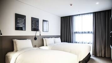 Habitación de hotel con dos camas, un ventanal con cortinas y un cuadro con frases motivadoras.