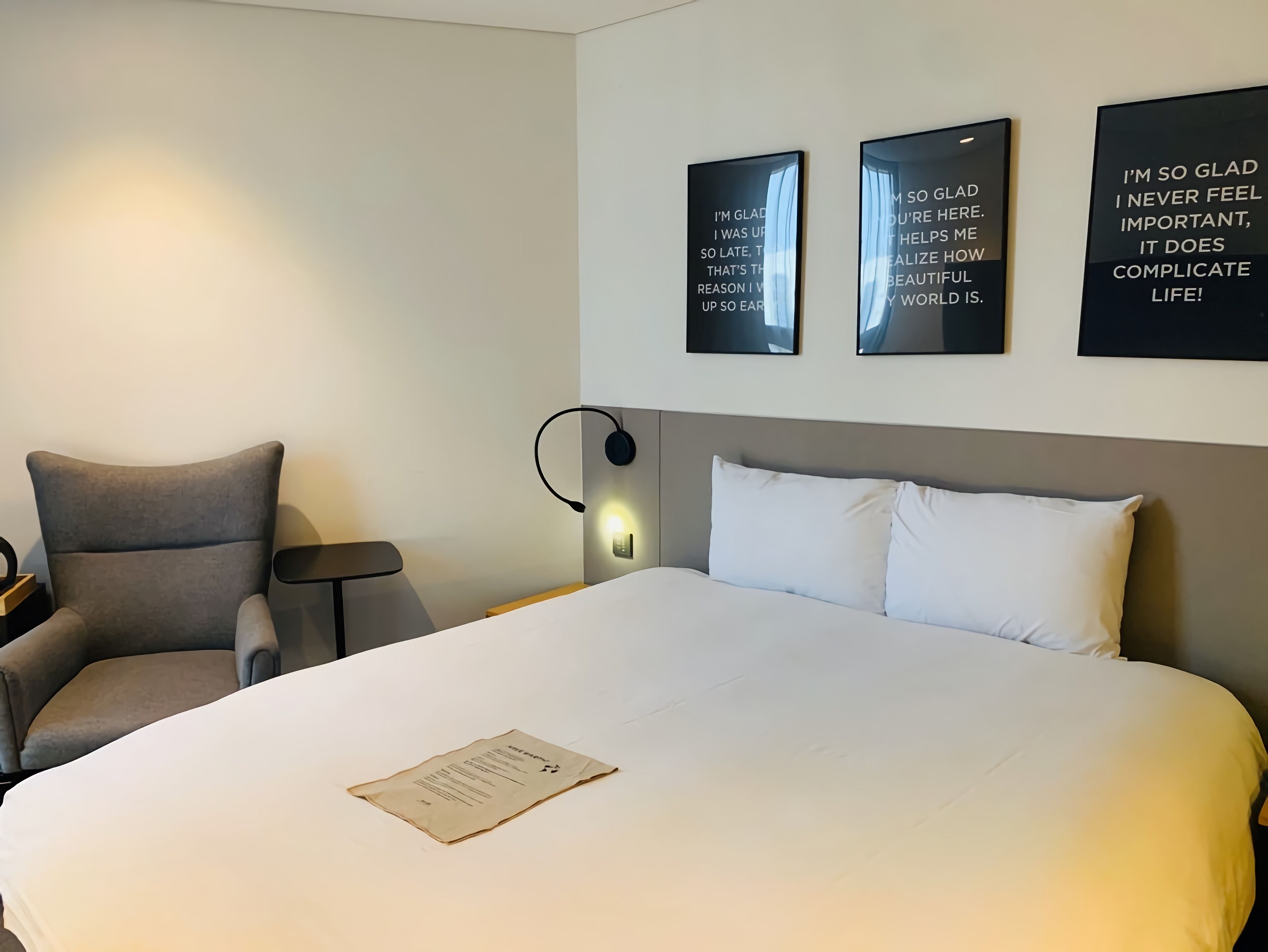 A hotel room with a large bed, a chair, a bedside table, and three motivational posters on the wall.
