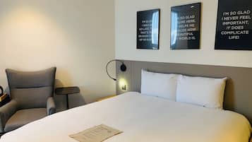 A hotel room with a large bed, a chair, a bedside table, and three motivational posters on the wall.