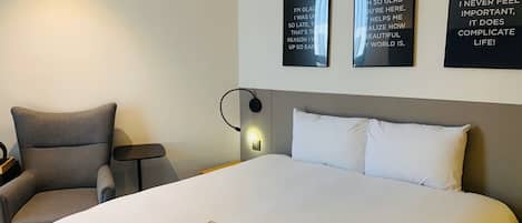A hotel room with a large bed, a chair, a bedside table, and three motivational posters on the wall.