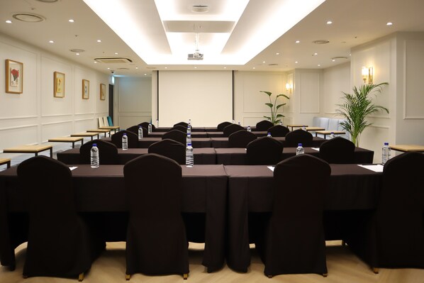 A conference room with multiple tables and chairs, equipped with water bottles, in a well-lit room with a projector and a large screen. - GLAD Gangnam COEX Center (Seoul)