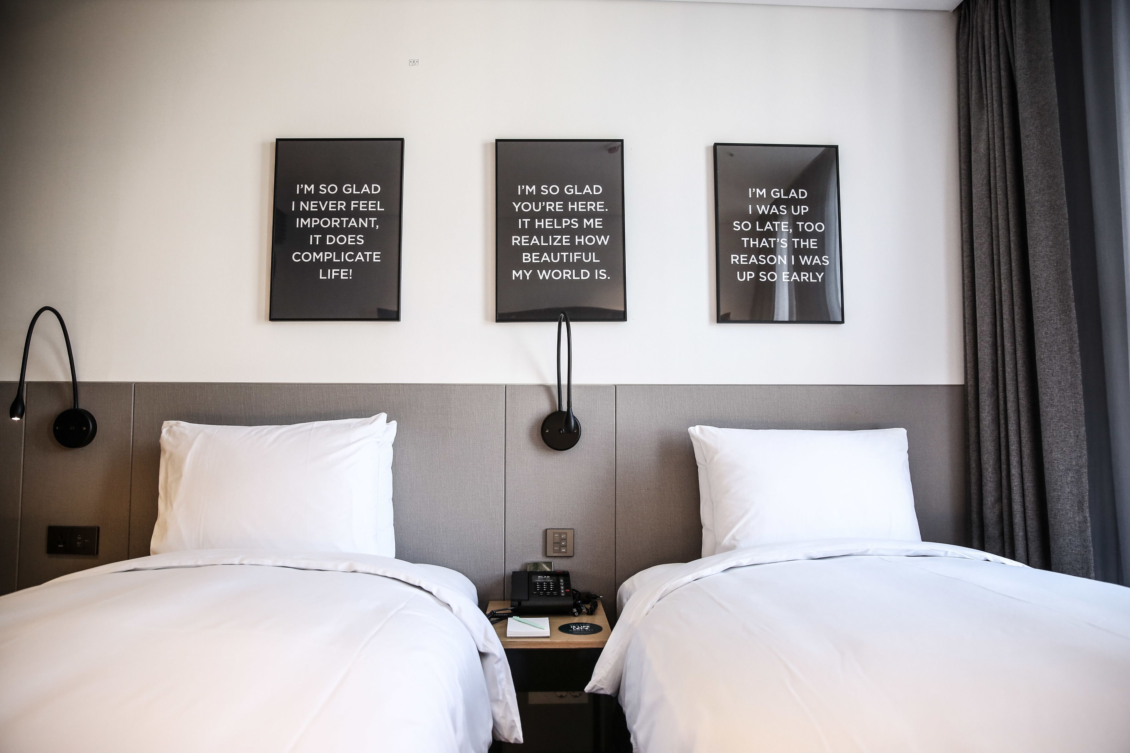 Ein Hotelzimmer mit zwei Betten, einem Nachttisch mit Telefon und drei motivierenden Wandbildern.