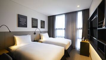 A hotel room with two beds, a desk, a TV, and three motivational wall art pieces.