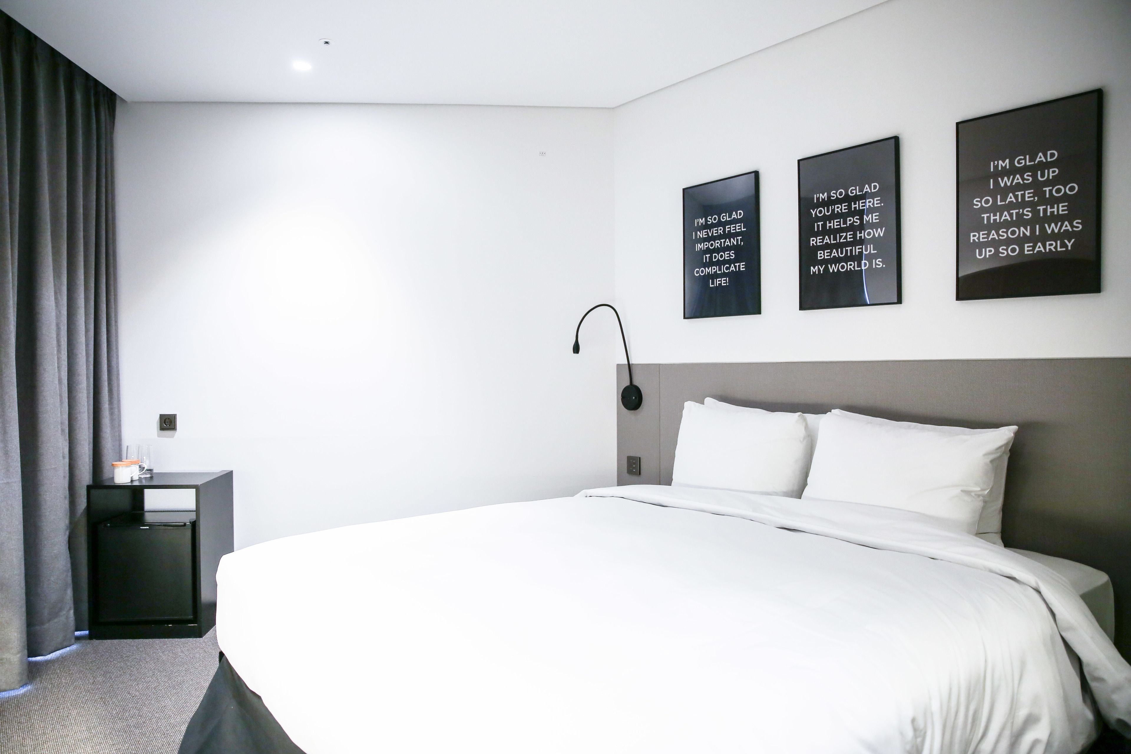 A hotel room with a large bed, a bedside table, a lamp, and three motivational posters on the wall.
