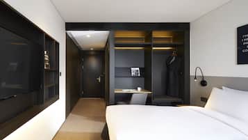A modern hotel room with a large bed, a desk with a chair, a wardrobe, and a television.
