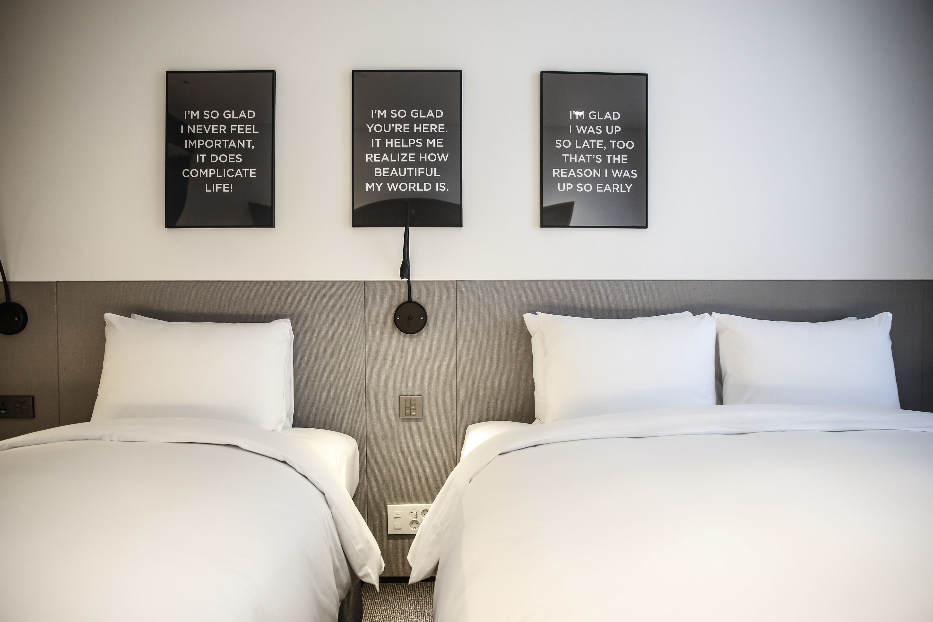 A hotel room with two beds, a neutral color scheme, and three motivational wall art pieces.