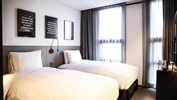 Habitación de hotel con dos camas, un escritorio y un ventanal con cortinas.