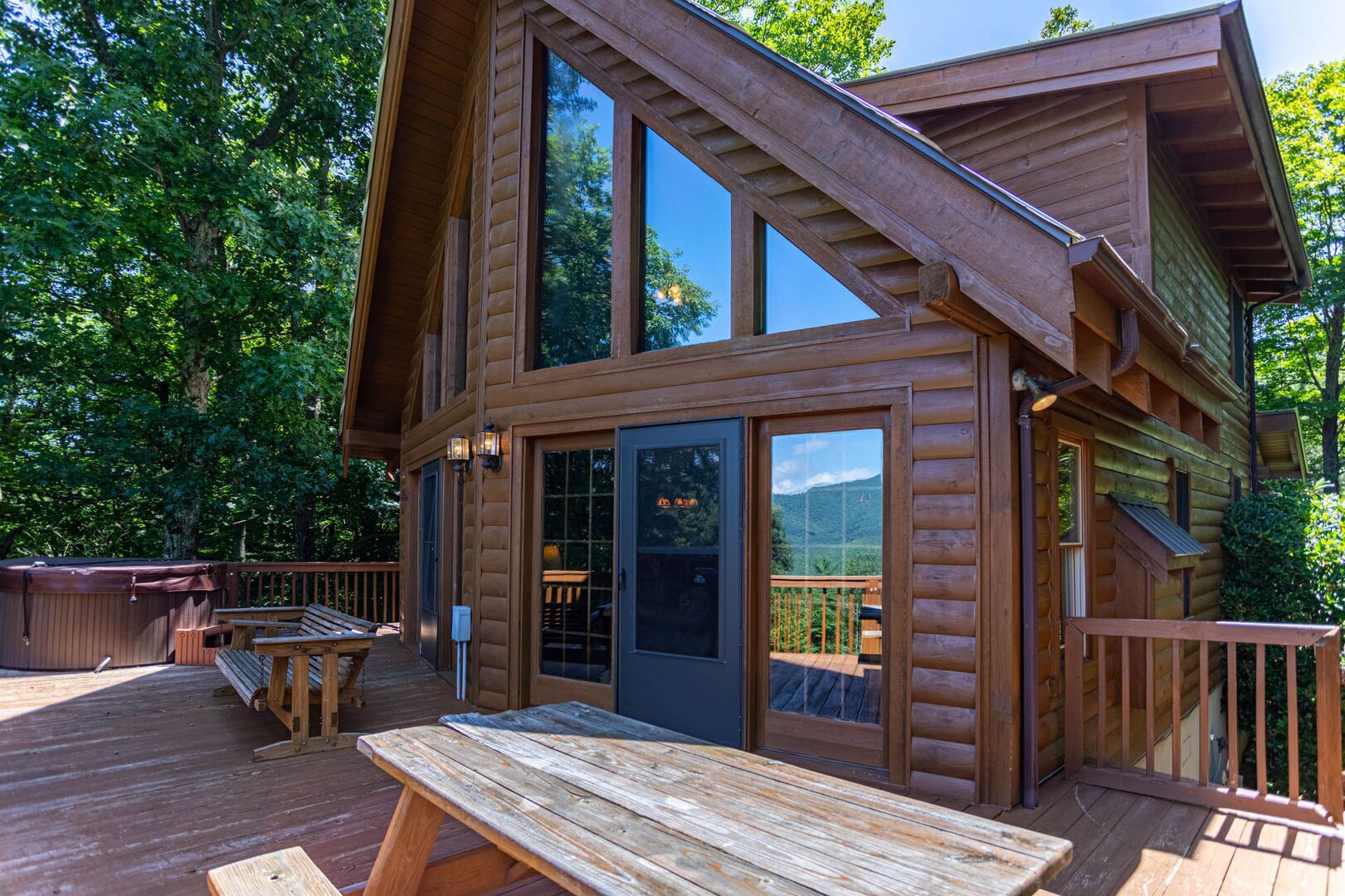 Una cabaña de madera con terraza, ventanas amplias y un jacuzzi.