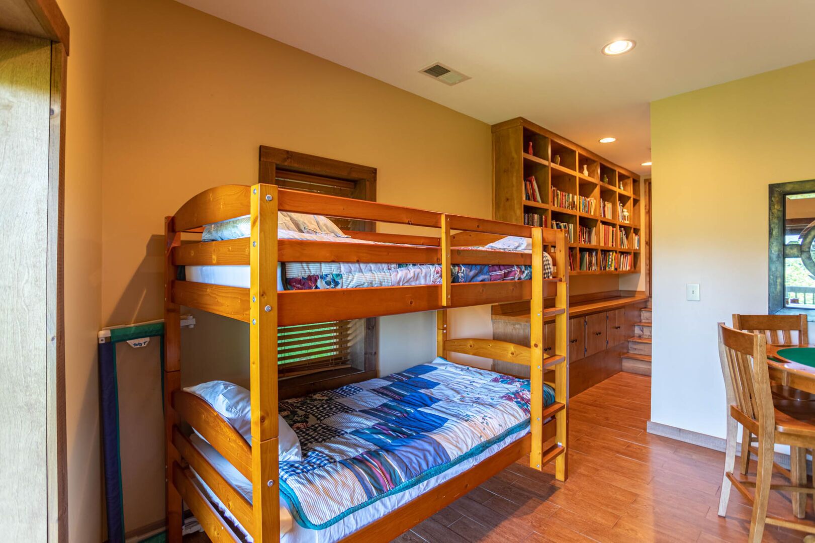 Une chambre avec un lit superposé, une bibliothèque en bois et une table à manger.