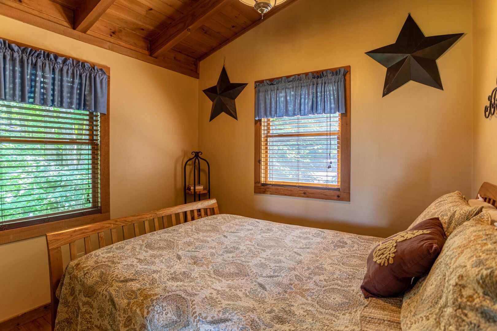 Un dormitorio con una cama grande, dos ventanas con cortinas, una decoración de estrellas en la pared y un cabecero de madera.