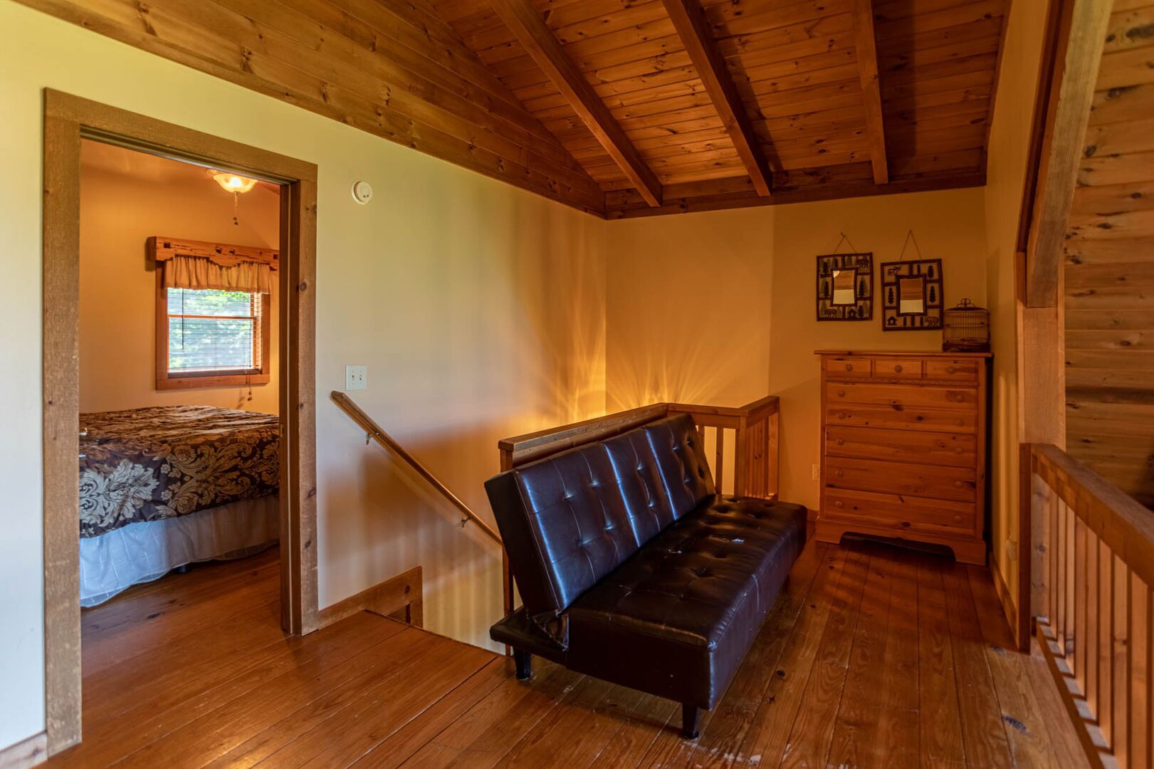A wooden-floored room with a black leather bench, a wooden dresser, and a bed with patterned bedding.