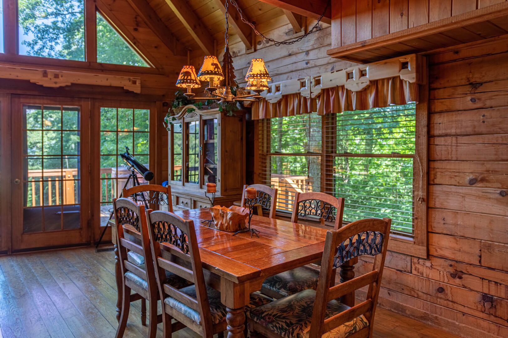 A wooden dining room with a large table and chairs, a chandelier, and large windows with curtains.
